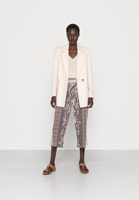 Blazer de linho bege claro com um único botão, combinado com calças cropped estampadas em tons de terra e sandálias rasas castanhas. Top de malha texturizada.