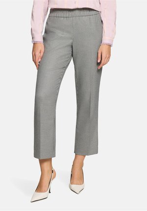 Woman wearing ankle-length black and white houndstooth pants, pale pink long-sleeve blouse, and white pointed high-heeled shoes.