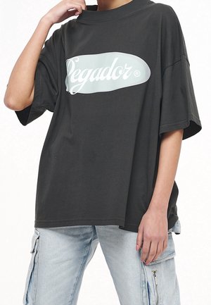 T-shirt nera oversize con logo verde menta "Segador" sul davanti. Collo tondo, maniche corte,Texture in cotone morbido, vestibilità rilassata.