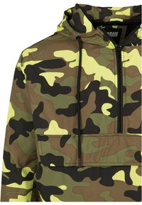 Lätt huva-pullover i kamouflage-mönster, med gröna, bruna och gula toner. Inkluderar justerbara snoddar och en framficka.