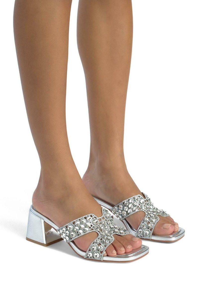 Zilveren sandalen met blokhak met een brede band versierd met grote heldere rhinestones. Openteen ontwerp met glanzende afwerking en textuuraccenten.