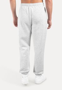 Grå bomullsmjukisbyxor med elastisk midja och muddar. Har en slät, texturerad yta och sidfickor. Bärs med vita sneakers.