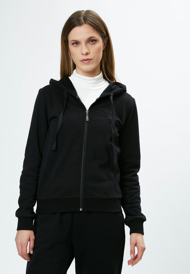 Hoodie nero con zip realizzato in tessuto morbido. Presenta un cappuccio, tasche frontali e polsini a coste. Design semplice con logo ricamato sul petto.