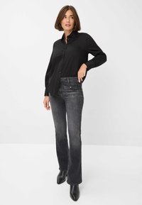 Chemise noire à boutons sur le devant avec manches longues, assortie à un jean évasé gris foncé et à des bottines noires à bout pointu. Tissu lisse, coupe ajustée.