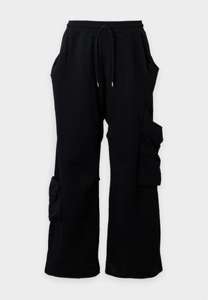 Jeune homme portant un polo rouge à manches longues et un pantalon cargo noir, se tenant devant un fond blanc uni.