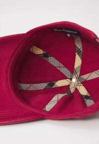 Casquette rouge avec une visière courbée. L'intérieur présente un motif à carreaux beige et noir avec des sangles. L'étiquette indique "Barbour" et précise "taille unique".