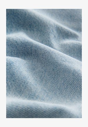 Lichtblau denim stof met een zachte textuur, die een subtiel twillpatroon en zachte plooien toont, wat de flexibele val benadrukt.