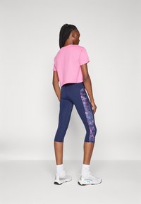 Pink cropped t-shirt paired with navy blue capri leggings featuring a colorful floral side panel. Model wearing white sneakers and socks.