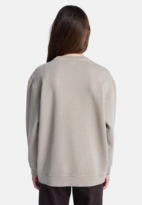 Oversized beige sweatshirt met een ronde hals, geribbelde manchetten en zoom. Zachte textuur met een gladde afwerking, ontworpen voor comfort.