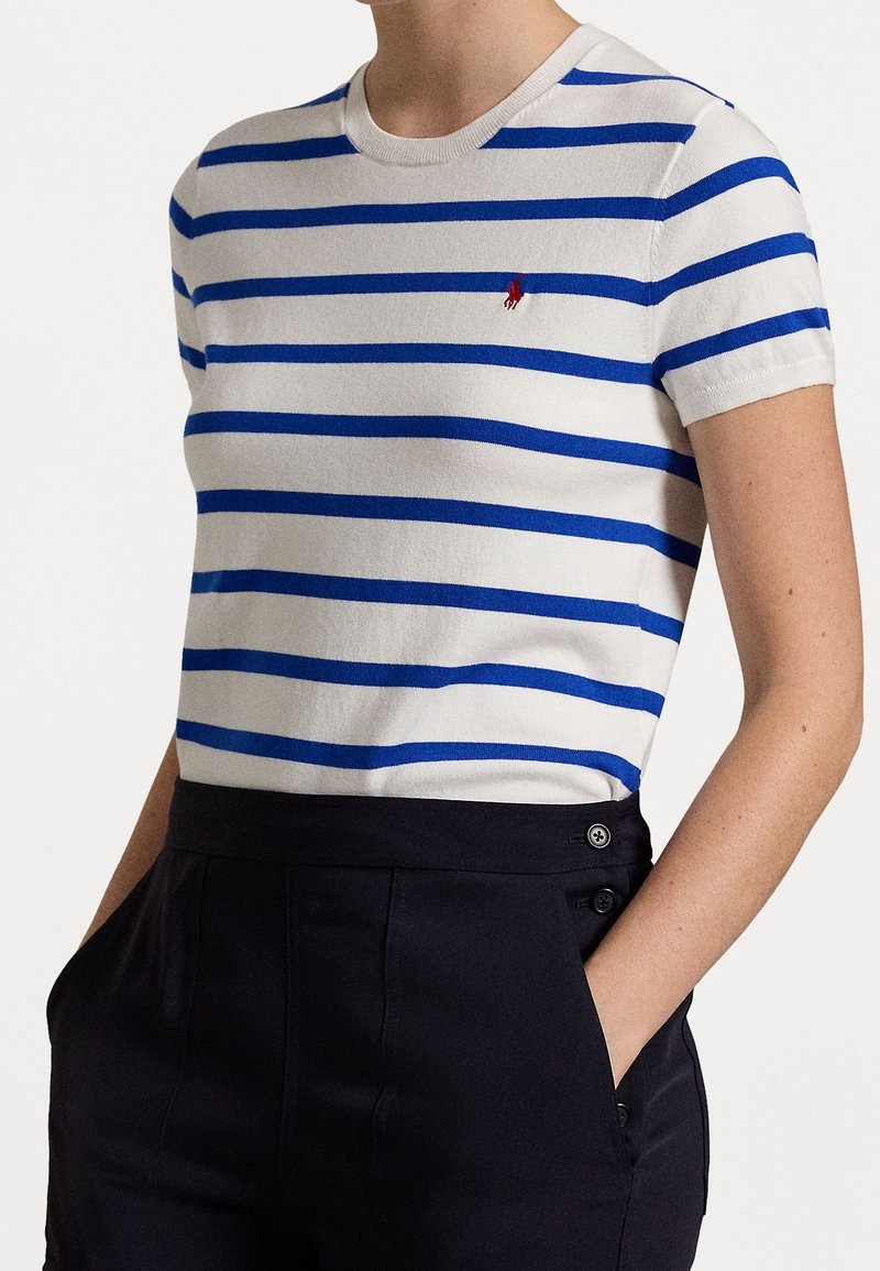 Biały T-shirt z krótkim rękawem z niebieskimi poziomymi paskami, z okrągłym dekoltem i małym czerwonym logo na lewej piersi.