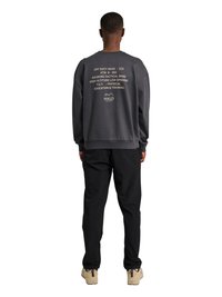 Osoba stoi tyłem do kamery, ubrana w ciemnoszarą bluzę z białym napisem odnoszącym się do "Aalborg Tactical Wing" oraz czarne spodnie.