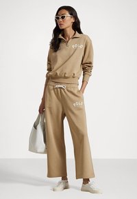 Bežinis zipas su kaklo megztinis su "POLO" logotipu, derinamas su atitinkamais platesniais džinsais. Skaidri medžiaga, raištelių juosta ir balti akcentai.