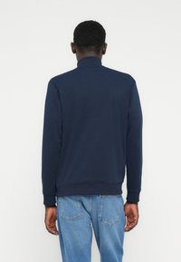 Μπλε σκούρο φούτερ με ψηλό γιακά και μακριά μανίκια, κατασκευασμένο από μαλακό ύφασμα. Διαθέτει ριγέ μανσέτες και τελείωμα, συνδυασμένο με ανοιχτόχρωμα τζιν.