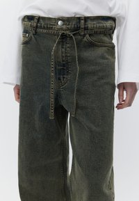 Olivengrønne denimbukser med en afslappet pasform, der har lukning med knapper foran, bæltestropper og en snørejustering i taljen.