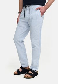 Pantalones de rayas azul claro y blanco con cintura ajustable, bolsillos y corte tapered. Combinados con sandalias negras.