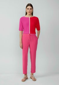 Korte mouw top in roze tinten met een witte naad, gecombineerd met roze broeken met een trekkoord in de taille en zijzakken. Sandalen als schoeisel.