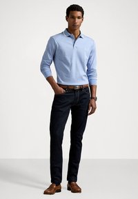 Ανοιχτό μπλε μακρυμάνικο πόλο πουκάμισο με γιακά και λευκή επένδυση, συνδυασμένο με σκούρο τζιν και καφέ μοκασίνια. Λεπτομερές ρολόι στον καρπό.