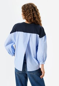Gestreifte blaue Bluse mit navyfarbenen Schultern, lässiger Passform, Ballonärmeln, abgerundetem Saum und einer Rückenbelüftung. Hergestellt aus leichtem Stoff.