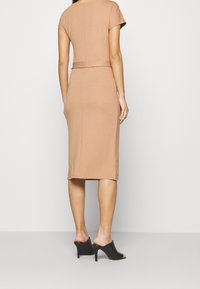 Robe midi ajustée en tissu jersey marron clair, avec des manches courtes et une coupe à la taille, associée à des talons ouverts noirs.