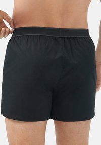 Pantaloni da bagno neri realizzati in materiale leggero, con cintura elastica e una consistenza liscia, progettati per offrire comfort e libertà di movimento.