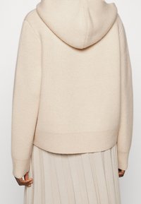 Hoodie aus weichem beigen Stoff; mit gerippten Bündchen und Saum, glatter Textur und lockerer Passform, kombiniert mit einem plissierten Rock.
