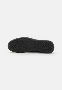 Black sneaker sole featuring a textured rubber outsole with a diamond pattern and a small blue logo emblem, providing traction and durability.