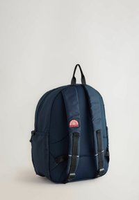 Zaino blu in nylon con superficie texturizzata, spallacci imbottiti, tasca frontale e una patch con logo. Presenta una maniglia superiore per il trasporto.