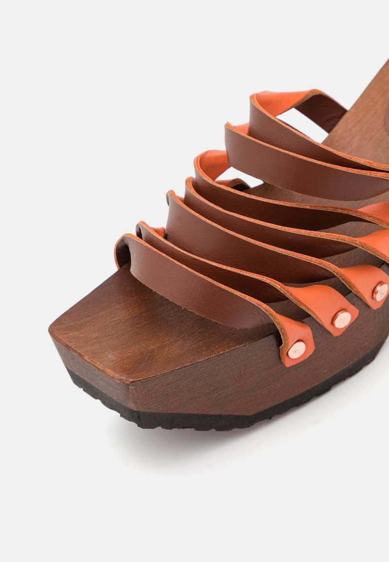 Holzplattform-Sandalette mit dunklem Holzsockel, braunen Lederriemen und orangen Akzenten. Runde Beschläge an den Seiten.