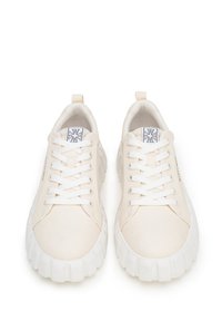 Zapatillas de lona blancas con puntera redonda, cordones planos y suela de goma texturizada. Presenta un parche con el logotipo en la lengüeta y una lengüeta en el talón.