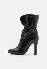 Μαύρη δερμάτινη μπότα στον αστράγαλο με χαλαρή περιφέρεια, μυτερή μύτη και ψηλό τακούνι στιλέτο. Λείος αφηρημένος σχεδιασμός με συγκεντρωμένες λε�πτομέρειες στον αστράγαλο.