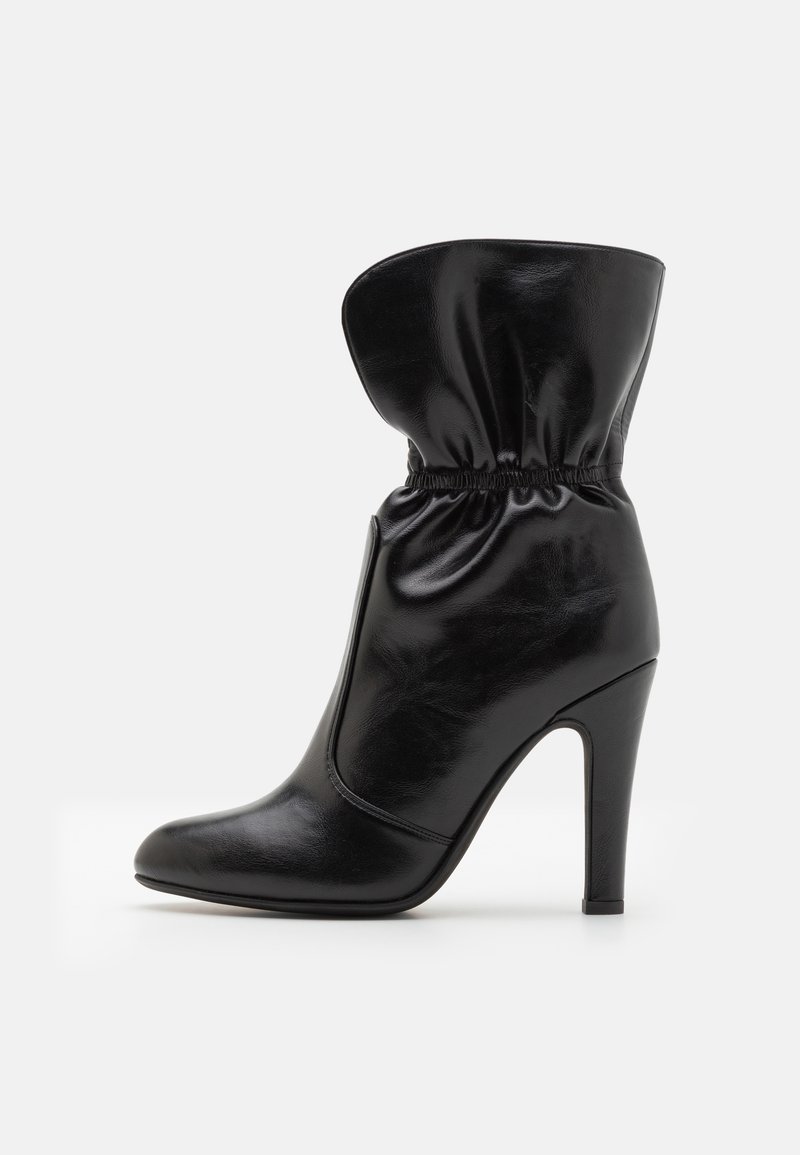 Μαύρη δερμάτινη μπότα στον αστράγαλο με χαλαρή περιφέρεια, μυτερή μύτη και ψηλό τακούνι στιλέτο. Λείος αφηρημένος σχεδιασμός με συγκεντρωμένες λεπτομέρειες στον αστράγαλο.