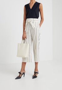 Haut sans manches noir avec décolleté en V ; pantalon taille haute à rayures blanches et beiges ; escarpins noirs à talons pointus avec accents ronds ; sac fourre-tout crème.