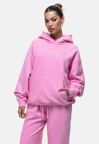 Felpa rosa realizzata in tessuto morbido, con tasca frontale e cappuccio regolabile con cordino. Caratteristiche notevoli includono una vestibilità ampia e un delicato dettaglio del logo.
