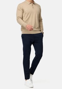 Suéter de polo de punto beige con cuello y tres botones, combinado con pantalones slim-fit de lana oscura y zapatillas blancas. Diseño sencillo, sin patrones.