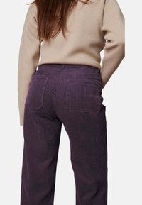 Paarse corduroy broek met verticale ribbelstructuur, twee achterzakken en een middelhoge taille, gecombineerd met een beige trui.