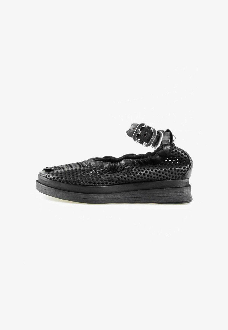 Chaussure en cuir noir perforé avec une semelle épaisse et une bride de cheville réglable avec boucle, présentée en profil latéral sur fond blanc.