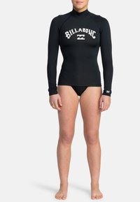 Černý rash guard s dlouhým rukávem a stojáčkem; má kontrastní bílé logo "Billabong" přes hruď a přiléhavý střih.