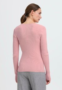 Langærmet ribbet sweater i lys pink, med en tætsiddende pasform og blød tekstur. Bagfra fremhæves strømlinede linjer og minimal detaljer.