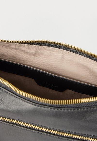 Κοντινό πλάνο ενός ανοιχτού μαύρου δερμάτινου τσαντιού που δείχνει το μπεζ υφασμάτινο εσωτερικό και τα χρυσά δόντια του φερμουάρ κατά μήκος του ανοίγματος.