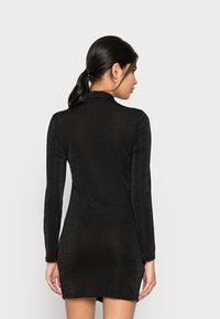 Vestido preto de mangas compridas feito de um tecido suave e texturizado, com um design ajustado que se estende logo acima da metade da coxa, apresentando um colarinho minimalista.