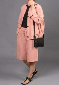 Chaqueta de lino rosa claro con botones negros combinada con pantalones cortos de lino a juego. Top negro debajo, bolso bandolera negro y sandalias negras.