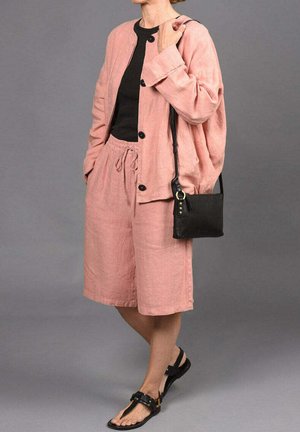 Chaqueta de lino rosa claro con botones negros combinada con pantalones cortos de lino a juego. Top negro debajo, bolso bandolera negro y sandalias negras.