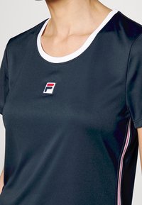 Námořnické sportovní tričko s kulatým výstřihem, bílým lemováním a malým logem. Má texturovanou látku a tenké akcentové pruhy po stranách.