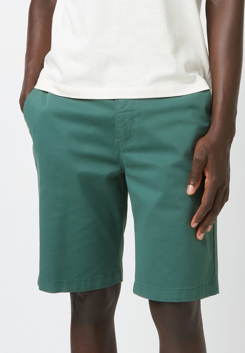 Shorts en coton vert avec une texture lisse, dotés de poches latérales et d'un design simple. Les shorts ont une coupe droite et un ourlet net.