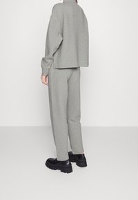 Personne portant un haut long à manches grises côtelé et un pantalon assorti, associé à des chaussures à plateforme noires, se tenant devant un fond blanc uni.