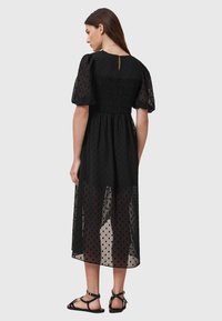 Vestido negro con tela de textura floral transparente, mangas cortas abullonadas y corsé fruncido. Presenta un abertura en la parte posterior en forma de llave y longitud hasta la mitad de la pantorrilla.