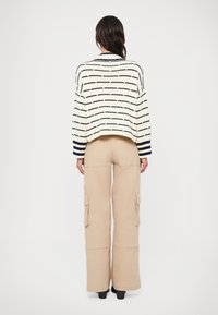 Kreminė ir tamsiai mėlyna raištinė megztinis derinamas su smėlio spalvos kargo kelnėmis, turinčiomis šonines kišenes ir plačią kojų dizainą.