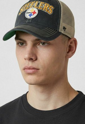 Junger Mann, der eine schwarz-beige Steelers-Baseballkappe und ein schwarzes Rundhals-Shirt trägt, schaut leicht zur Seite mit neutralausdruck.