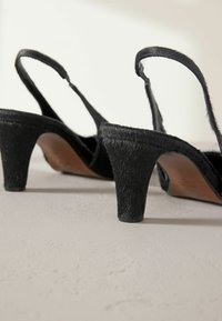 Čierne slingback opätky s textúrovaným povrchom pripomínajúcim kožušinu, krátkymi blokovými podpätkami a minimalistickým dizajnom. Hladký interiér s koženými akcentmi.