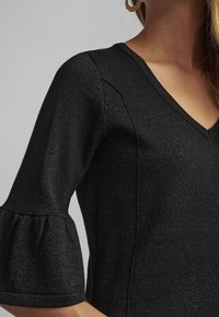 Svart stickad topp med V-ringning, utställda kortärmar och ett strukturerat mönster med en subtil glanseffekt.